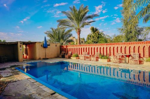 a swimming pool next to a brick wall with palm trees at Tebtunis in ‘Izbat an Nāmūs