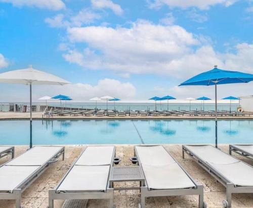 a swimming pool with benches and umbrellas on the beach at Charming seaside studio for 4 people! - Rate included resort fee-Parking fee not included- in Sunny Isles Beach