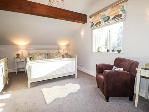 a bedroom with a crib and a chair and a window at Peony Cottage in Ulverston