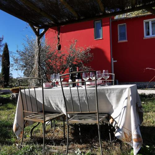 a table with wine glasses on it in front of a red house at Poggio la Luna - La casa nel vigneto in Montemerano