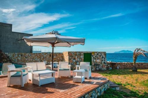 a patio with an umbrella and chairs and the ocean at Dar el haouaria in El Haouaria