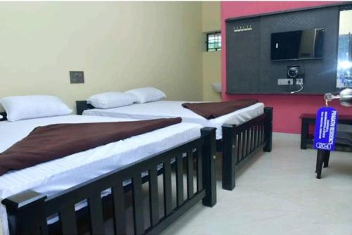 two beds in a room with a tv on the wall at Pragathi Residency in Dharmastala