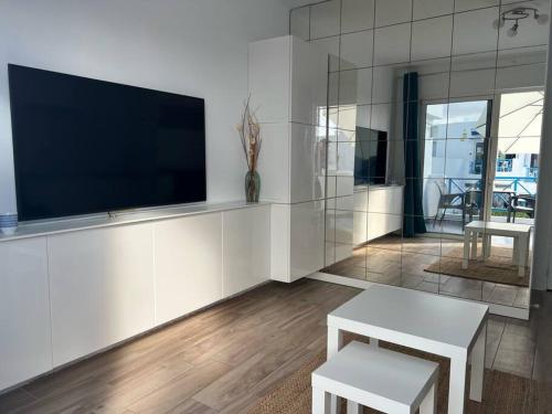 ein Wohnzimmer mit einem Flachbild-TV und 2 weißen Bänken in der Unterkunft 26 Puerto del Carmen Palm tree in Puerto del Carmen