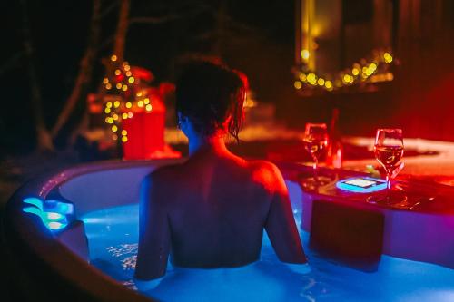 BRENDIS -'Virš Ąžuolų' - Forest SPA - FREE jacuzzi في Paplatelė: شخص يجلس في حوض الاستحمام مع كؤوس النبيذ