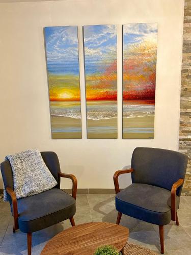 deux chaises et une table dans une pièce avec trois tableaux dans l'établissement Cosy village house with home cinema, à Grandcamp-Maisy