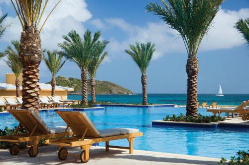 a pool with palm trees and chairs and the ocean at JW Marriott St Maarten Beach Resort & Spa in Dawn Beach