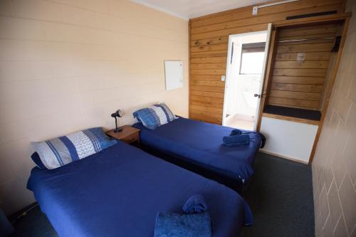 two beds in a room with blue sheets and a window at Bay of Islands Lodge in Paihia
