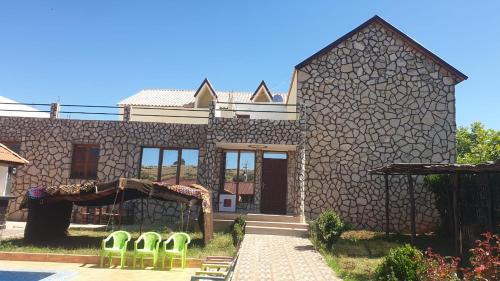 una casa de piedra con sillas verdes frente a ella en Auberge belle vue itto A Station de sevice ZIZ, en Aït nʼTaleb Akka