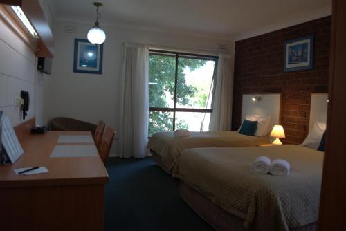 a hotel room with two beds and a desk and a window at City Gardens Motel in Traralgon