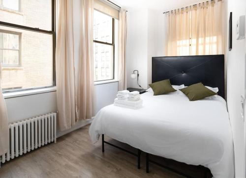 1 Schlafzimmer mit einem großen weißen Bett und 2 Fenstern in der Unterkunft Luxury 2BD nr Wall St Gym Rooftop w/d in New York