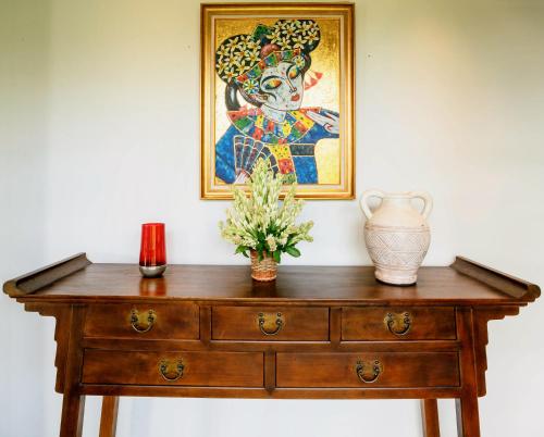 a wooden table with a vase and a painting on the wall at Villa Pulung Jimbaran by Nakula in Jimbaran