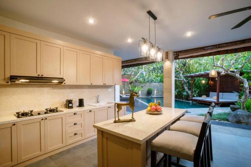 a kitchen with white cabinets and a table with a bowl of fruit at Villa Pulung Jimbaran by Nakula in Jimbaran