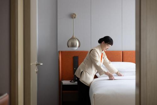 a woman making a bed in a hotel room at Home2 Suites By Hilton Hotel Guangzhou Baiyun International Airport Branch - Free Shuttle Bus to Guangzhou Baiyun International Airport & Free Deliver Service to Canton Fair Complex During Canton Fair Period in Huadu