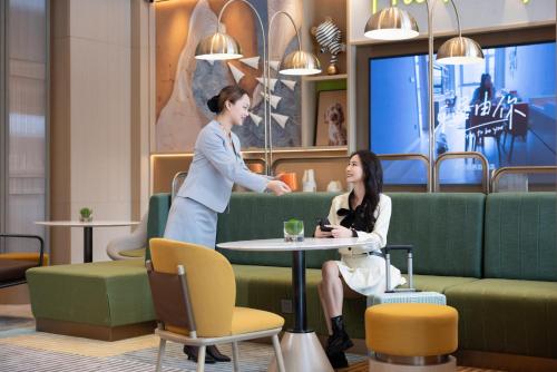 a woman is talking to a woman in a restaurant at Home2 Suites By Hilton Hotel Guangzhou Baiyun International Airport Branch - Free Shuttle Bus to Guangzhou Baiyun International Airport & Free Deliver Service to Canton Fair Complex During Canton Fair Period in Huadu