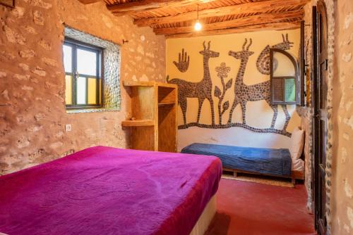 a bedroom with a bed with purple sheets and giraffes on the wall at Dar Afoulky Maison D'hotes in Sidi Kaouki