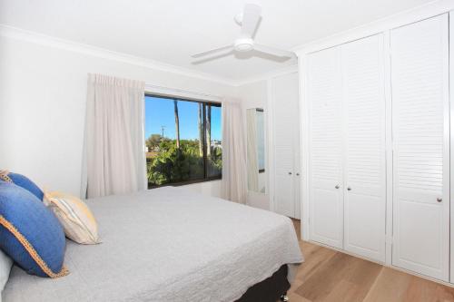 a white bedroom with a bed and a window at Windmill 3 in Mooloolaba