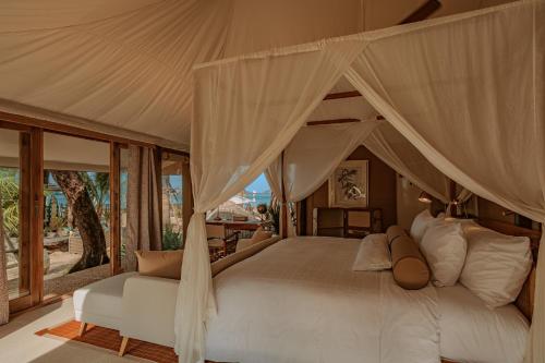 バンタオビーチにあるThe Lazy Coconut Glampingのベッドルーム(天蓋付きベッド1台、白いソファ付)