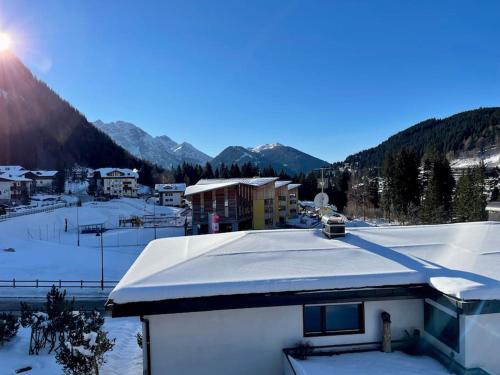 un tetto innevato di un edificio con montagne sullo sfondo di Grazioso appartamento a Madonna di Campiglio a Madonna di Campiglio