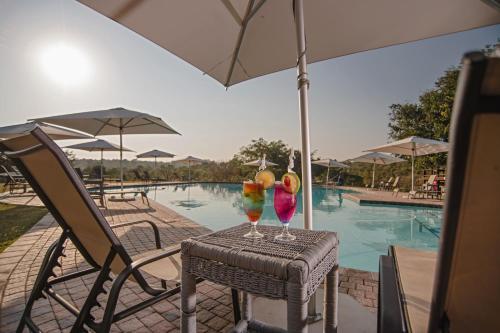 two cocktails sitting on a table next to a swimming pool at Nkambeni Safari Camp in Hazyview