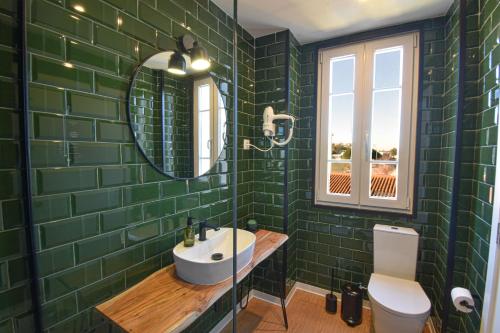 uma casa de banho com azulejos verdes, um lavatório e um espelho. em ArchiSuites em Coimbra