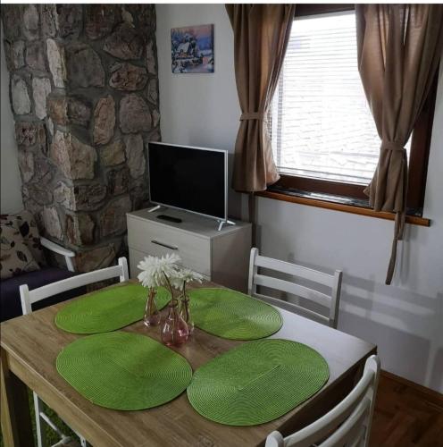 einen Esstisch mit grünen Kissen und einen TV in der Unterkunft Apartman Miloš na Kopaoniku in Raška