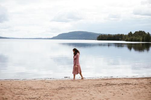 a woman walking on the beach near a body of water at STF Undersvik Gårdshotell & Vandrarhem in Vallsta