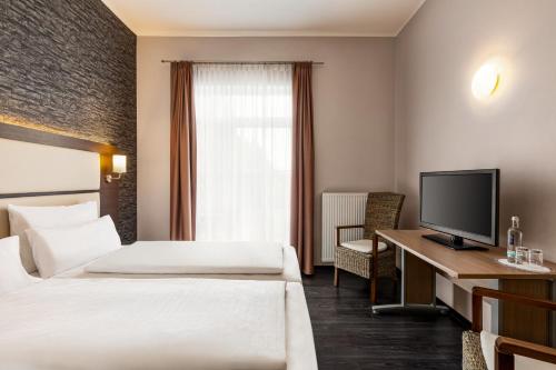 a hotel room with two beds and a desk with a television at Amedia Express Bielefeld, Trademark Collection by Wyndham in Werther