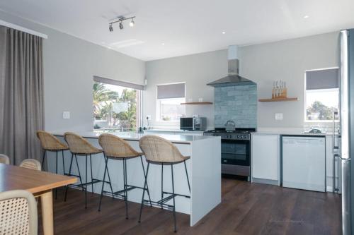 a kitchen with white counters and stools and a table at Blue Bay Lodge in Saldanha