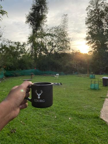 una mano che tiene una tazza di caffè con un cane sopra di Greenhouse Homestay a Siddapur