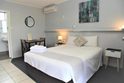 a bedroom with a large white bed and a bathroom at Charm City Motel in Bundaberg