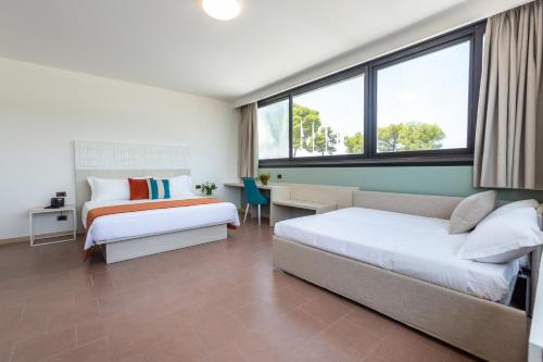 a bedroom with two beds and a desk and window at Porto Giardino - CDSHotels in Monopoli
