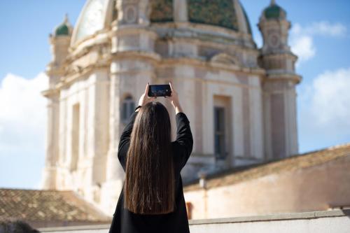 a woman taking a picture of a building with her cell phone at ZIBIBBO SUITES & ROOMS - Aparthotel in Centro Storico a Trapani in Trapani