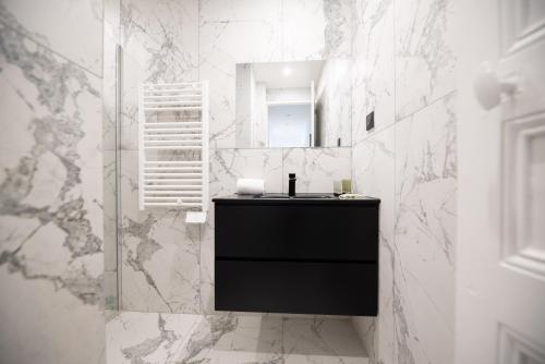 La salle de bains est pourvue d'un lavabo noir et de murs en marbre blanc. dans l'établissement Vignature REIMS - Cathédrale, à Reims