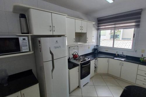 a kitchen with white cabinets and a white refrigerator at Condominio Agua Marinha, Praia Brava; 3 quartos, frente mar, in Florianópolis