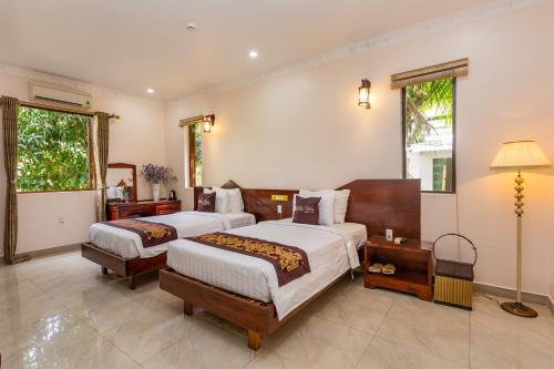 a bedroom with two beds and a desk and two windows at Phu Van Resort & Spa in Phu Quoc
