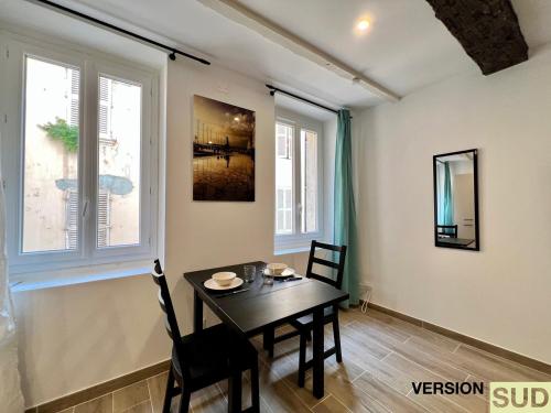 una sala da pranzo con tavolo e sedie e due finestre di Version SUD : Cosy appartement centre ville a Tolone