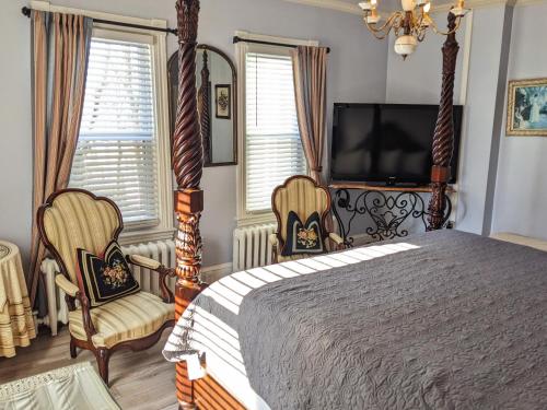a bedroom with a bed and two chairs and a television at Chelsea Pub and Inn in Atlantic City