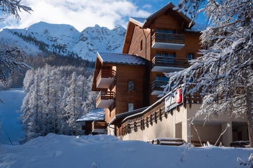 a building covered in snow with mountains in the background at Résidence Pierre & Vacances l'Albane in Vars