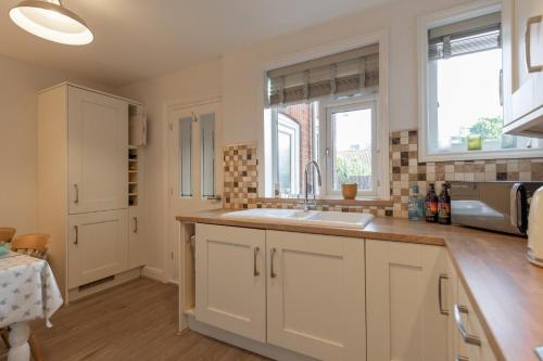 eine Küche mit weißen Schränken, einem Waschbecken und 2 Fenstern in der Unterkunft 17 St Edmunds Road in Southwold
