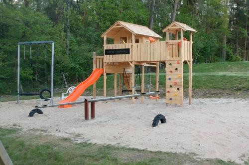 a playground with a wooden play structure and a slide at Camping Sonnenberg in Faßberg