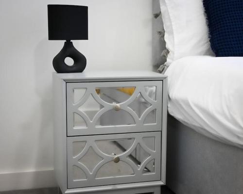 a white nightstand with a lamp on it next to a bed at Chic 1 Bedroom Flat in Bedford