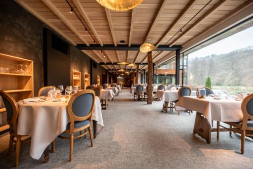um restaurante com mesas e cadeiras brancas e uma grande janela em Logis Hostellerie De La Claire Fontaine em La-Roche-en-Ardenne