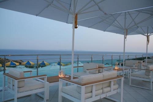 a balcony with white chairs and umbrellas and the ocean at Princessa Riviera Resort in Pythagoreio