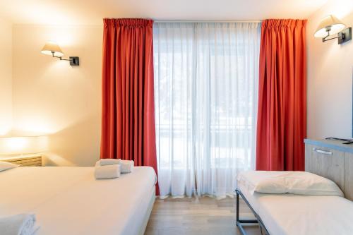 a bedroom with two beds and a window with red curtains at Gressoney Saint-Jean apartments by Halldis in Gressoney-Saint-Jean