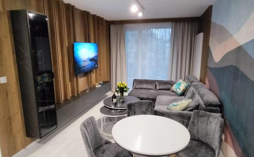 een woonkamer met een bank, een tafel en een tv bij Cicha Przystań Apartamenty WhiteBlue sauna&fitness&parking in Kołobrzeg