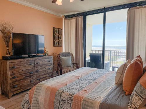 ein Schlafzimmer mit Bett, Fernseher und Balkon in der Unterkunft 604 Holiday Isle Beach Life in Dauphin Island