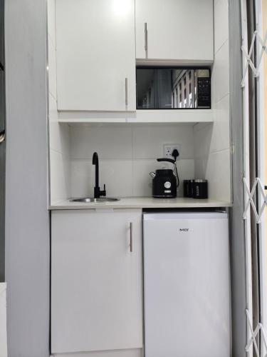 uma cozinha branca com armários brancos e um lavatório em Vusi's Guesthouse em Durban