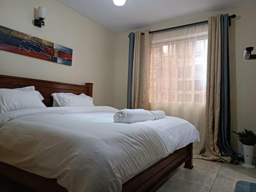 a bedroom with a bed with white sheets and a window at Lux Suites Neema Court Furnished Apartments in Nairobi