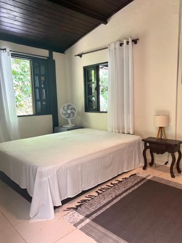 a bedroom with a large bed with white sheets and windows at Flor da Mata in São Sebastião