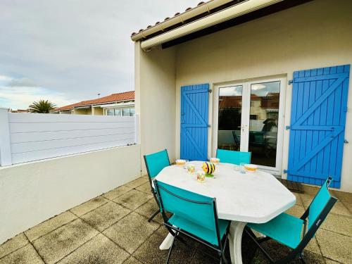 une table et des chaises sur une terrasse avec portes bleues dans l'établissement Jolie maison de vacances mitoyenne au calme proche Tanchet 4 personnes, à Les Sables-dʼOlonne